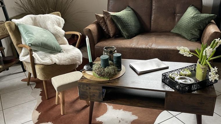 Ein gemütliches Wohnzimmer mit einem braunen Ledersofa und einem bequemen Stuhl. Auf dem Tisch stehen Dekorationen und eine kleine Pflanze.