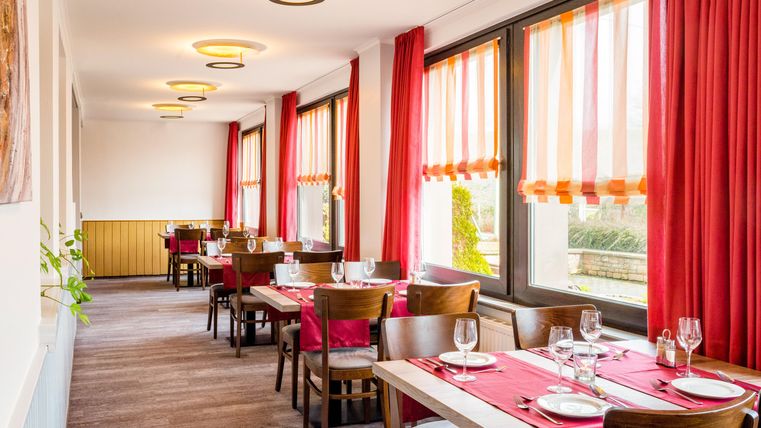 Ein einladendes Restaurant mit Holzstühlen und rot-weiß gestreiften Vorhängen. Die Tische sind elegant gedeckt und bieten einen Blick nach draußen.