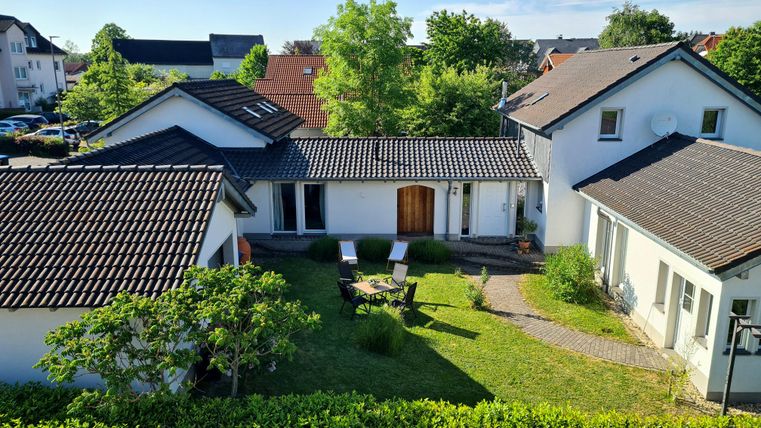 Ein ruhiger Innenhof mit einem gepflegten Garten und zwei Liegestühlen. Im Hintergrund sind moderne Wohnhäuser und eine grüne Umgebung sichtbar.