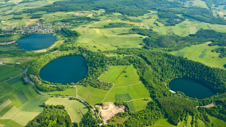 Eine weitläufige Landschaft mit grünen Feldern und zwei blauen Seen. Die Umgebung ist hügelig und reich an Bäumen.