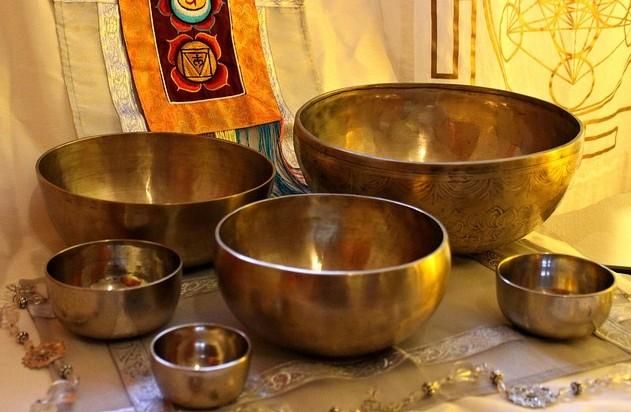 Eine Reihe von verschiedenen Schalen aus Metall, die in unterschiedlichen Größen angeordnet sind. Im Hintergrund sind dekorative Textilien und Symbole zu sehen.