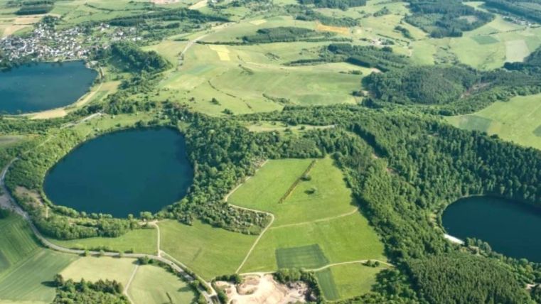 Eine weitläufige Landschaft mit mehreren Seen und hügeligen Feldern. Grünes Gelände und Wälder prägen die Umgebung.