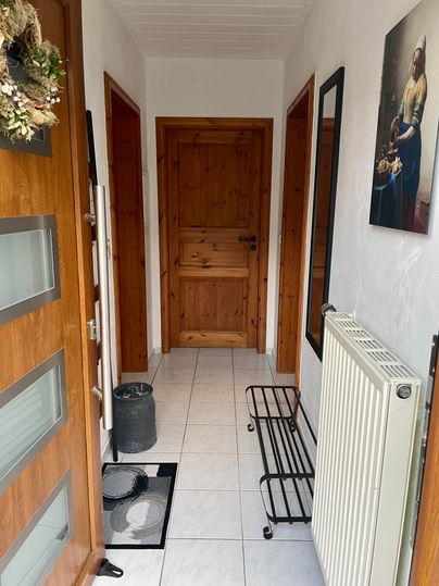 Ein heller Flur mit Holzdetails und einem großen Spiegel. In der Ecke befindet sich ein Heizkörper und eine Schuhablage.
