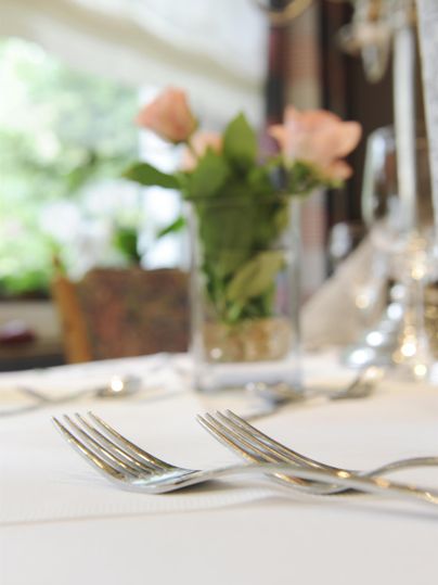 Ein elegant gedeckter Tisch mit zwei Gabeln und einer kleinen Vase mit rosa Rosen. Im Hintergrund ist eine grüne Umgebung sichtbar.