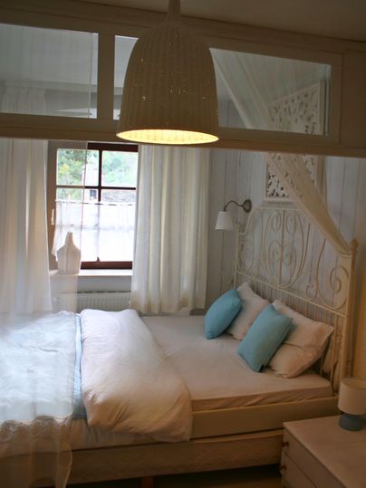 Ein gemütliches Schlafzimmer mit einem großen Bett und hellen Vorhängen. Die Einrichtung ist einfach und modern, mit einer schönen Pendelleuchte und Dekor in sanften Farben.