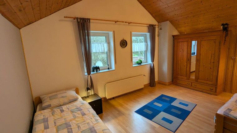 Ein gemütliches Schlafzimmer mit zwei Einzelbetten und Holzwänden. Die Fenster sorgen für viel natürliches Licht und der Teppich verleiht dem Raum eine warme Atmosphäre.