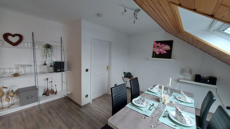 Ein gemütlicher Essbereich mit einem modernen Tisch und Stühlen. An der Wand hängt ein Bild einer Blume, und das Zimmer ist hell und freundlich eingerichtet.