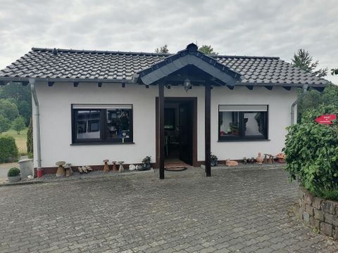 Ein gemütliches Haus mit einem schwarzen Dach und weißen Wänden. Der Eingangsbereich ist von einer gepflasterten Fläche umgeben.