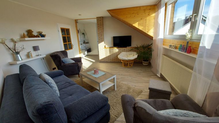 Ein gemütliches Wohnzimmer mit einer modernen Einrichtung. Es gibt ein Sofa, einen Couchtisch und große Fenster, die viel Licht hereinlassen.