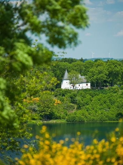 A white building with towers is picturesque by a lake, surrounded by green nature. The scene radiates calm and tranquility.