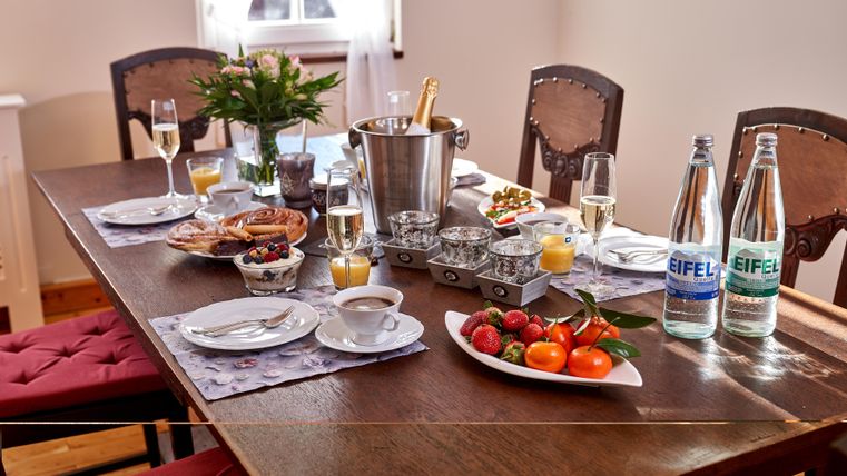 Ein schön gedeckter Tisch mit Glaswaren, Obst und Snacks. Im Hintergrund stehen eine Flasche Sekt und Mineralwasser.