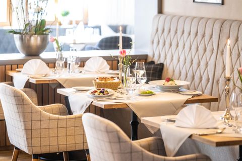 Ein elegantes Restaurant mit stilvollen Tischen und bequemen Stühlen. Die Tischdekoration umfasst Blumen und gedecktes Geschirr, was eine angenehme Atmosphäre schafft.