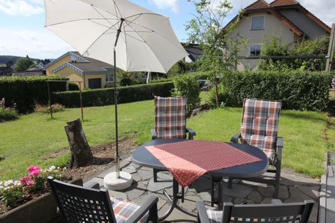 Ein gemütlicher Garten mit einem Tisch und Stühlen. Ein Sonnenschirm bietet Schatten, während die grüne Umgebung einladend wirkt.