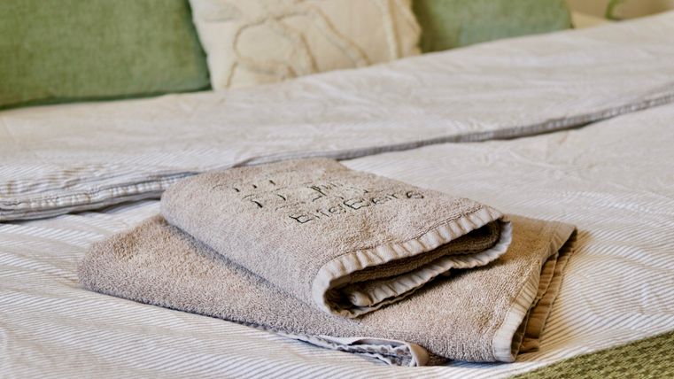Ein Bett mit gestreifter Bettwäsche und dekorativen Kissen. Darauf liegen ordentlich gefaltete Handtücher.