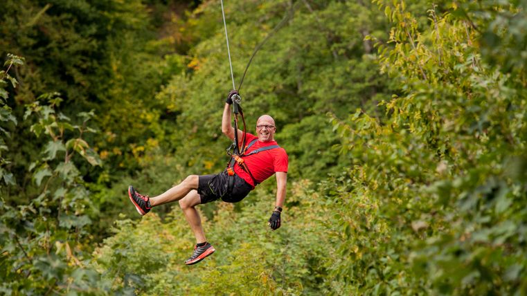 Person in a red shirt on a zipline above a green forest.