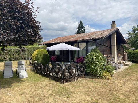 Ein hübsches Holzhaus mit einem gepflegten Garten. Im Vordergrund stehen Liegen und ein Tisch mit einem Sonnenschirm.