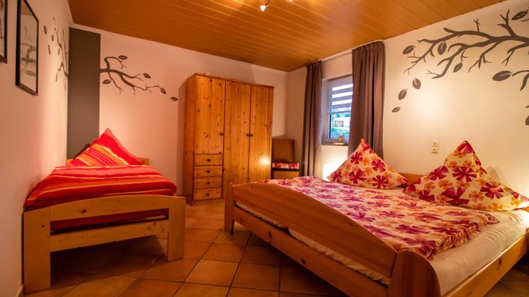 Ein gemütliches Schlafzimmer mit einem Doppelbett und einem Einzelbett. Die Einrichtung ist aus Holz und die Wände sind dekoriert.