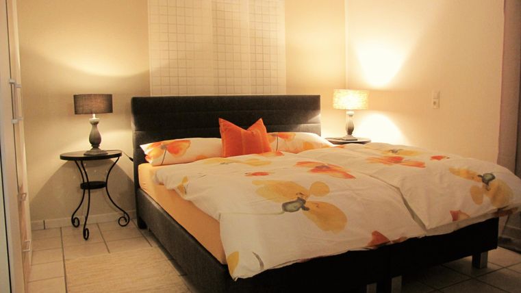 Ein gemütliches Schlafzimmer mit einem großen Bett und einer bunten Bettdecke. Neben dem Bett stehen Nachttische mit Lampen.
