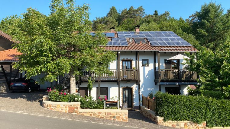Ein modernes Haus mit Solarpanelen auf dem Dach. Es steht in einer ruhigen Umgebung mit grünen Bäumen und einem gepflegten Garten.