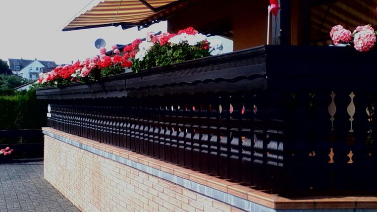 Ein schöner Balkon mit bunten Blumenkästen. Die Terrasse hat eine elegante Holzbrüstung und ist von einer sonnigen Umgebung umgeben.