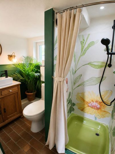 Ein modernes Badezimmer mit einer Dusche und bunten Wandmalereien. Im Hintergrund stehen eine Pflanze und ein Holzschrank.