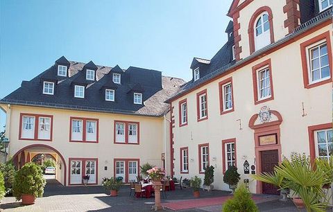 Ein historisches Gebäude mit roter und gelber Fassade. Der sonnige Innenhof ist mit Pflanzen und Außensitzgelegenheiten ausgestattet.