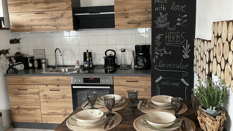 Eine moderne Küche mit Holzregalen und einem Essbereich. Der Tisch ist gedeckt mit Geschirr und dekorativen Pflanzen.
