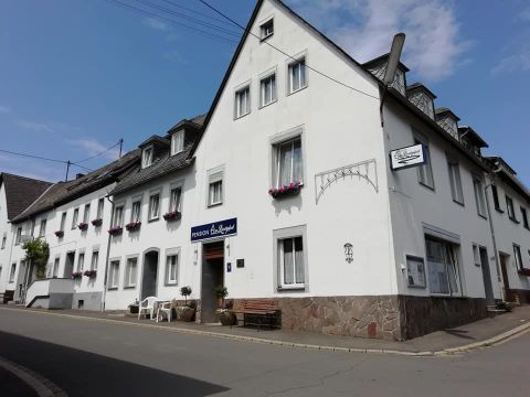 Ein weißes Gebäude mit mehreren Fenstern und Blumenkästen. Vor dem Haus stehen Stühle und ein Tisch auf der Straße.