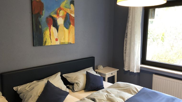 Ein gemütliches Schlafzimmer mit einem großen Bett und buntem Kunstwerk an der Wand. Der Raum ist hell und freundlich, mit einem Fenster und einer Lampe, die für angenehmes Licht sorgen.