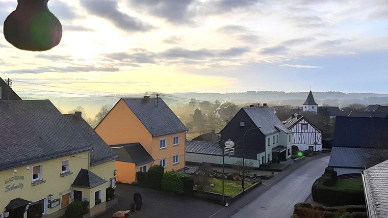 Ein malerisches Dorf mit bunten Häusern und sanften Hügeln im Hintergrund. Der Himmel ist bewölkt und strahlt ein sanftes Licht aus.
