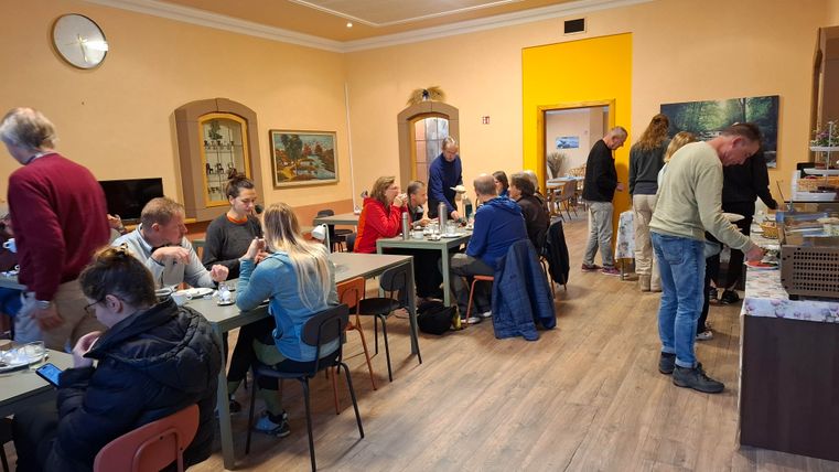 Ein gemütlicher Raum mit mehreren Tischen, an denen Menschen zusammen essen und sich unterhalten.