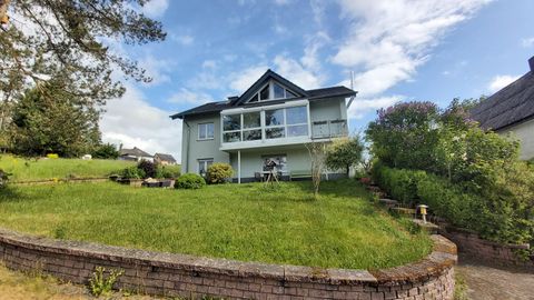 Ein schönes Haus mit einem großen Garten und viel Grün. Der Himmel ist klar und es gibt einige Bäume in der Umgebung.