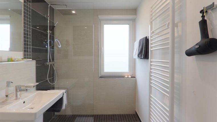 Ein modernes Badezimmer mit einer Dusche aus Glas und einer weißen Waschtischanlage. Der Raum ist hell und minimalistisch gestaltet.