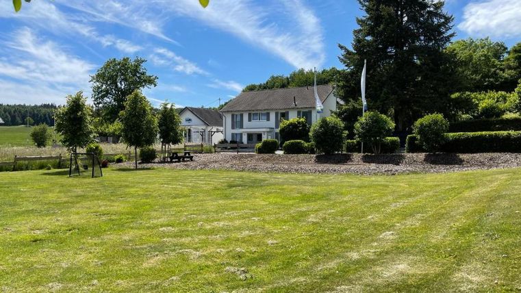 Ein schönes Anwesen mit einem großen, grünen Garten. Im Hintergrund sieht man ein modernes Haus umgeben von Bäumen und Sträuchern.