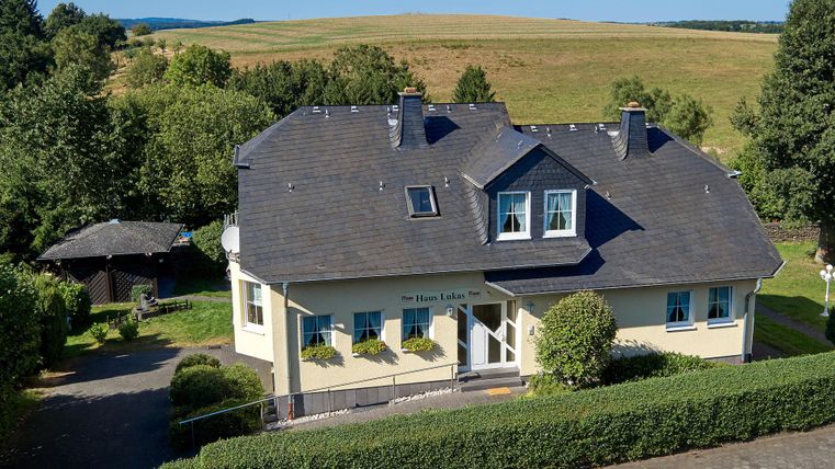 Ein modernes Haus mit einem schön angelegten Garten. Im Hintergrund sind grüne Felder und ein klarer Himmel zu sehen.