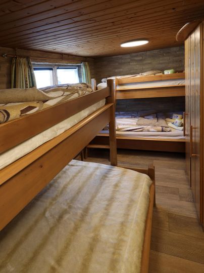 Ein gemütlicher Schlafraum mit Etagenbetten aus Holz. Der Raum hat eine warme Atmosphäre durch die Holzverkleidung und das natürliche Licht.