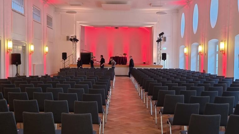 Ein modernes Gebäude mit Holzverkleidung und großen Fenstern. Der Eingangsbereich ist einladend gestaltet und von einem gepflasterten Platz umgeben.