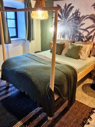 Ein modernes Schlafzimmer mit einem Doppelbett und einem gemütlichen Teppich. Die Wände sind mit Palmenmotiven dekoriert, und es gibt stilvolle Fenster mit Vorhängen.