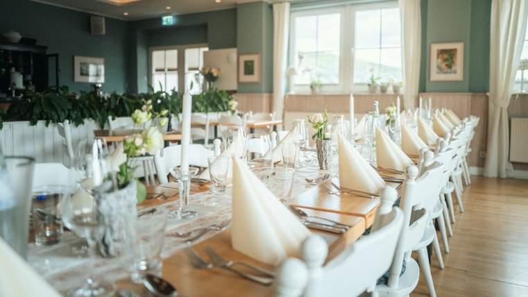 Ein elegant gedeckter Tisch in einem hellen Restaurant mit schönen Blumen und Kerzen. Die Atmosphäre wirkt einladend und geschmackvoll.