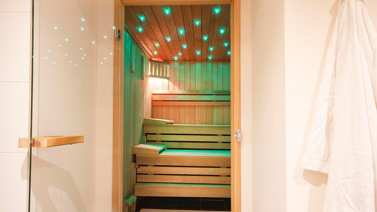 Eine moderne Sauna mit Holzregalen und stimmungsvollem Licht. Die Glastür bietet einen Blick auf den warmen Innenraum.