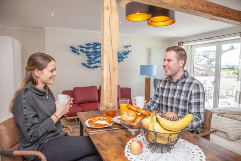 Een gezellige ontbijttafel met verse broodjes, fruit en dranken. Twee lachende personen genieten samen van hun tijd in een lichte ruimte.
