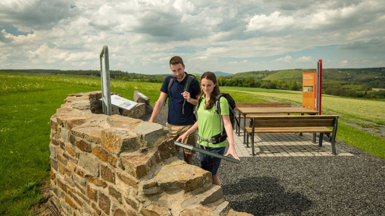 Two hikers look at an information board at a Roman villa ruin on a hiking trail.
