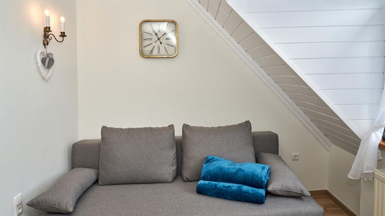 Ein gemütliches Wohnzimmer mit einem grauen Sofa und blauen Kissen. An der Wand hängt eine Uhr und es gibt sanfte Beleuchtung.