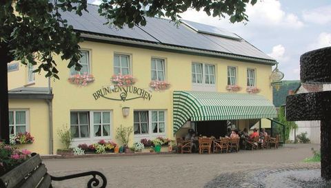 Een gezellig herberg met een gele gevel en kleurrijke bloemen. Het terras is voorzien van stoelen en tafels, ideaal voor gasten.