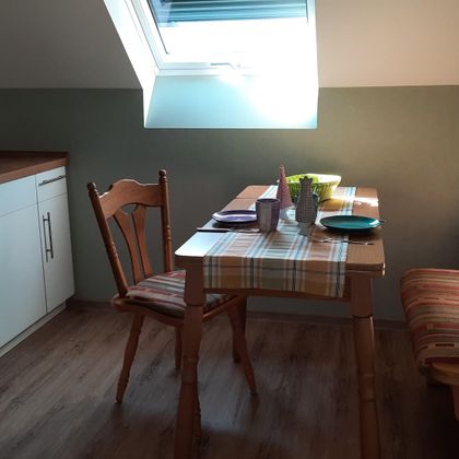 Eine gemütliche Küche mit einem kleinen Essbereich. Der Tisch ist gedeckt und das Licht fällt durch ein Fenster auf die Möbel.