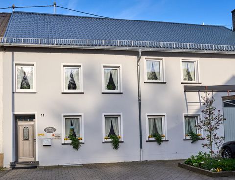 Een helder, modern huis met duidelijke raampartijen en groene planten voor de ramen. De lucht is blauw en het lijkt zonnig te zijn.