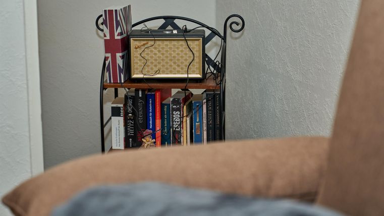 Ein gemütlicher Wohnbereich mit einem Bücherregal und einer Vintage-Box. Im Hintergrund ist eine britische Flagge zu sehen.