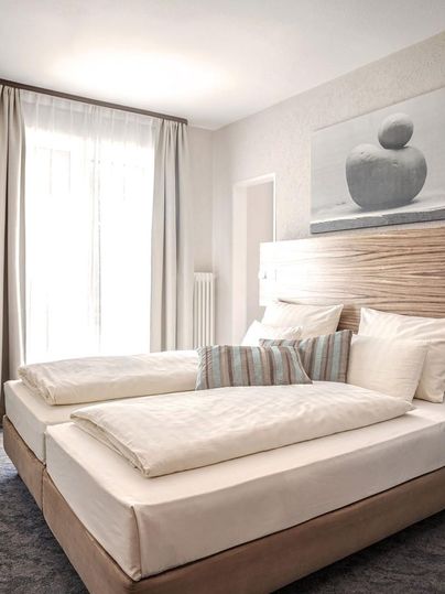 Ein helles und modernes Schlafzimmer mit zwei Einzelbetten. Die Einrichtung ist schlicht und elegant, mit einem Fenster, das viel Tageslicht hineinlässt.