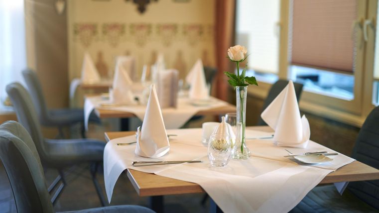 Ein elegant dekorierter Tisch in einem Restaurant mit weißen Tischdecken und Stoffservietten. Eine einzelne Rose in einer Vase ergänzt die stilvolle Atmosphäre.
