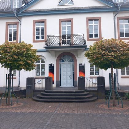 A historic building with a blue front door and symmetrical windows.
In front of the building stand two neatly trimmed trees.